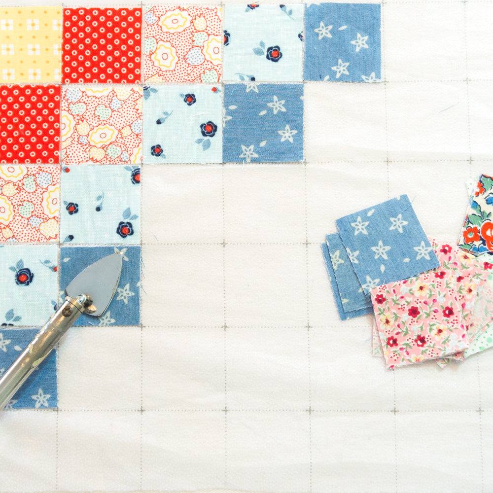 Easy Piecing Grid with colorful fabric squares and pressing tool for quilting craft.