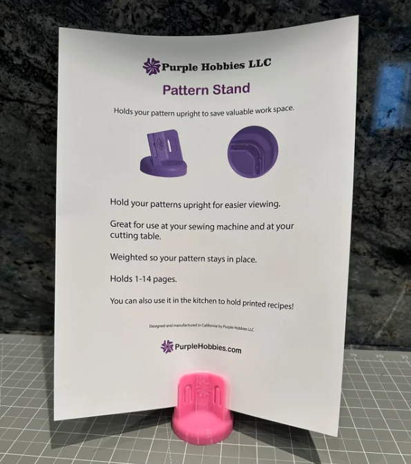 Pattern Stand Pink by Purple Hobbies LLC holding sewing patterns upright with weighted base for hands-free viewing