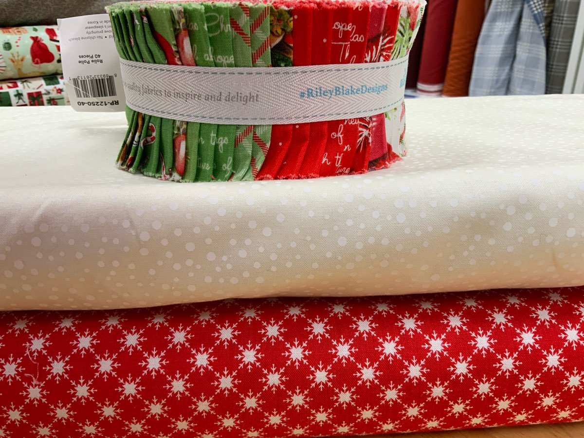 Project Jelly Roll Kit with red and green Christmas-themed fabric strips and coordinating white and red snowflake fabrics for Shift Quilt Kit