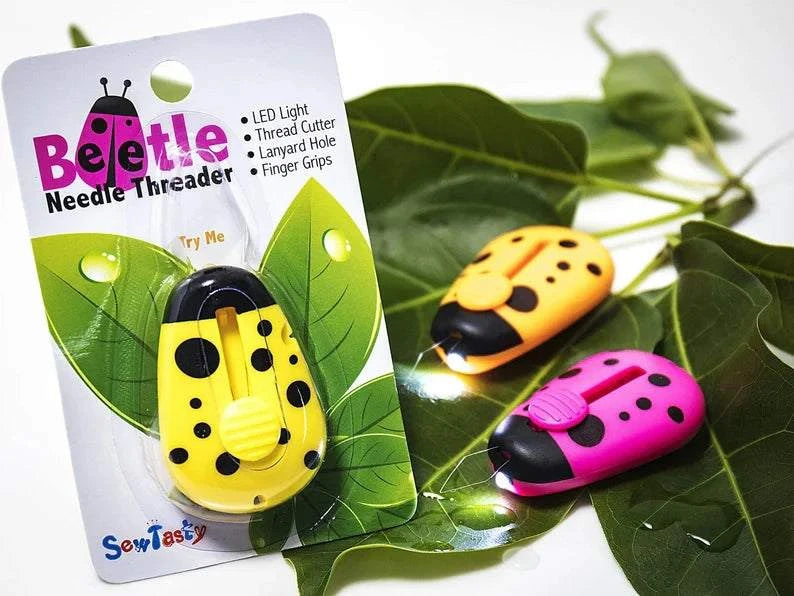 Beetle Needle Threader set with LED light, thread cutter, and lanyard hole in yellow, red, and green colors on green leaves