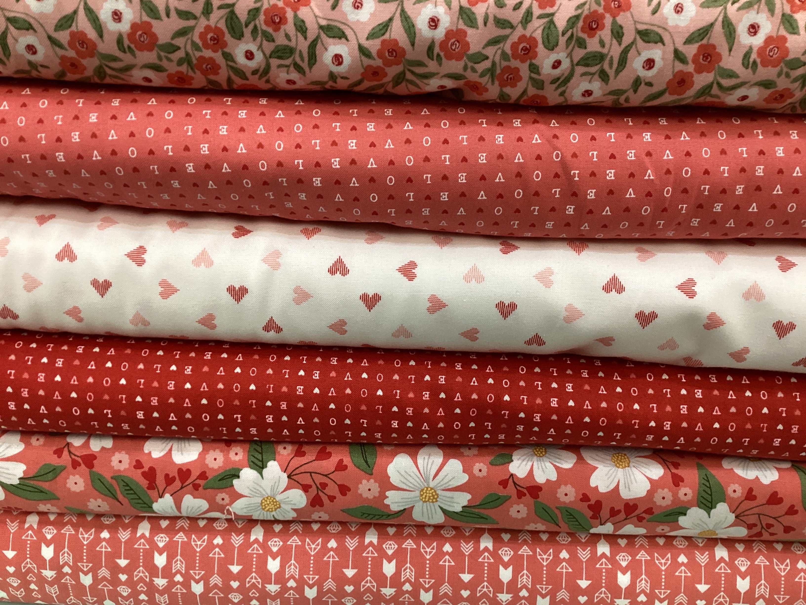 Stack of five cotton fabrics in red and white with floral, heart, and geometric patterns from M50 Lucky Break Kit curated by Bella Rose Quilts