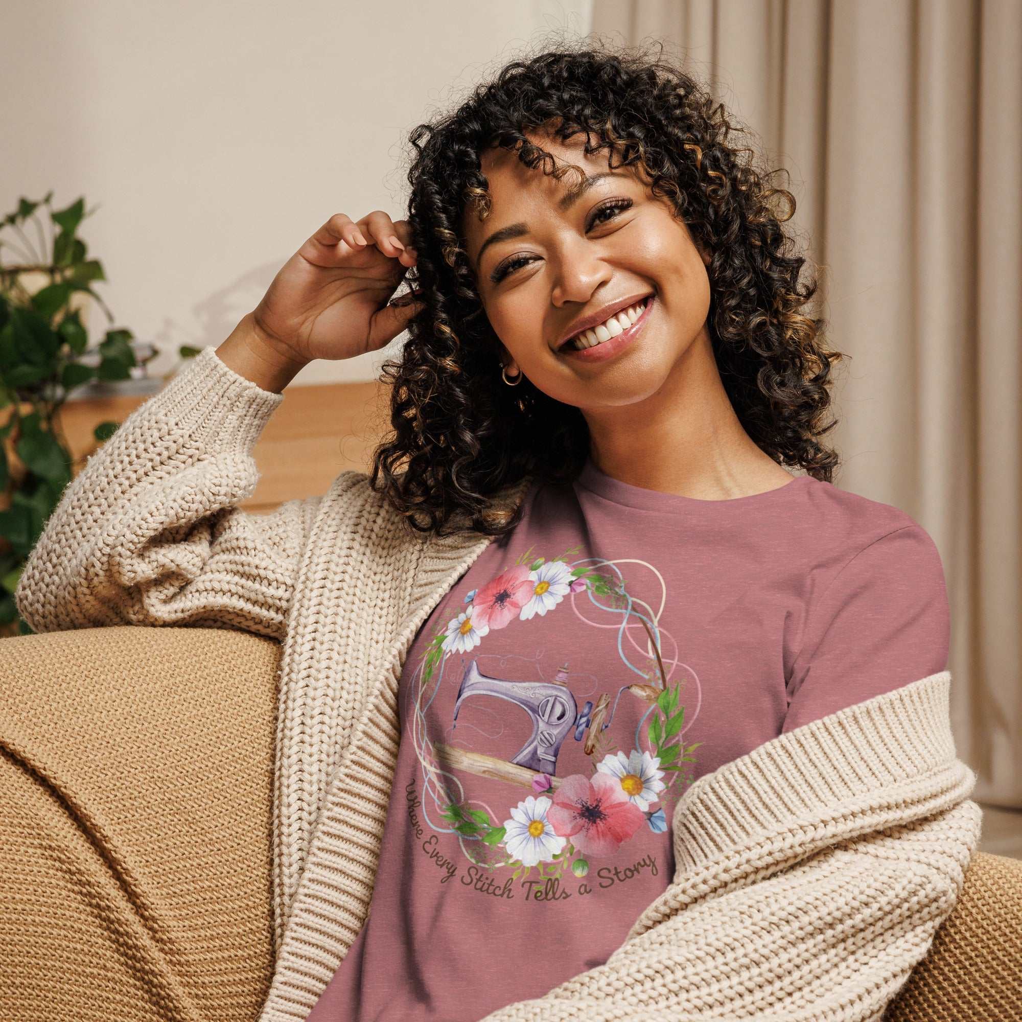 Smiling woman wearing a relaxed fit purple women's t-shirt with a sewing machine and flowers graphic, cozy beige cardigan, indoors