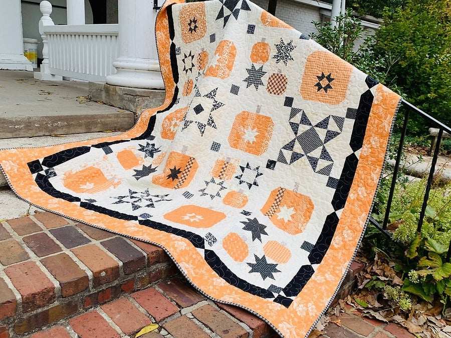 Star of the Patch quilt with orange, black, and white star and patch patterns draped on brick steps outdoors