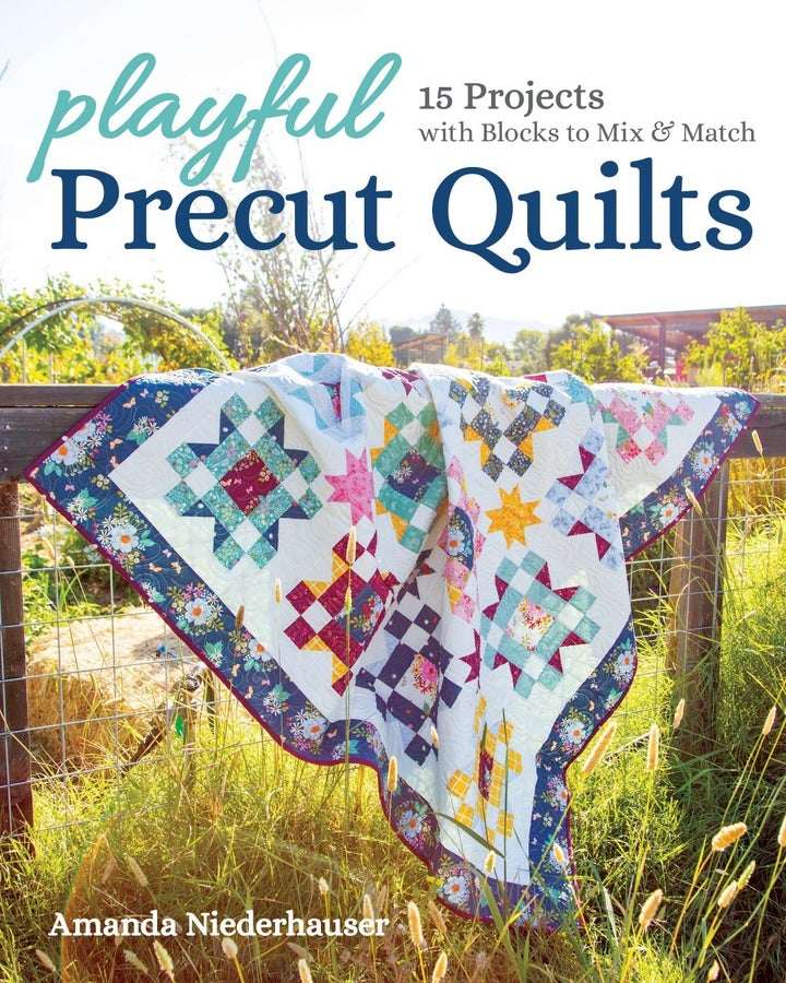 Colorful playful precut quilts draped on fence in sunlit field