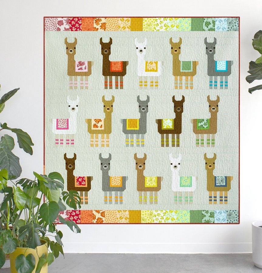 Little Llamas Quilt Kit featuring colorful llama pattern quilt with rainbow border hanging on wall