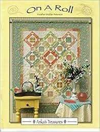 On A Roll Quilt Pattern featuring a patchwork quilt with pastel colors displayed above a yellow table with decorative items
