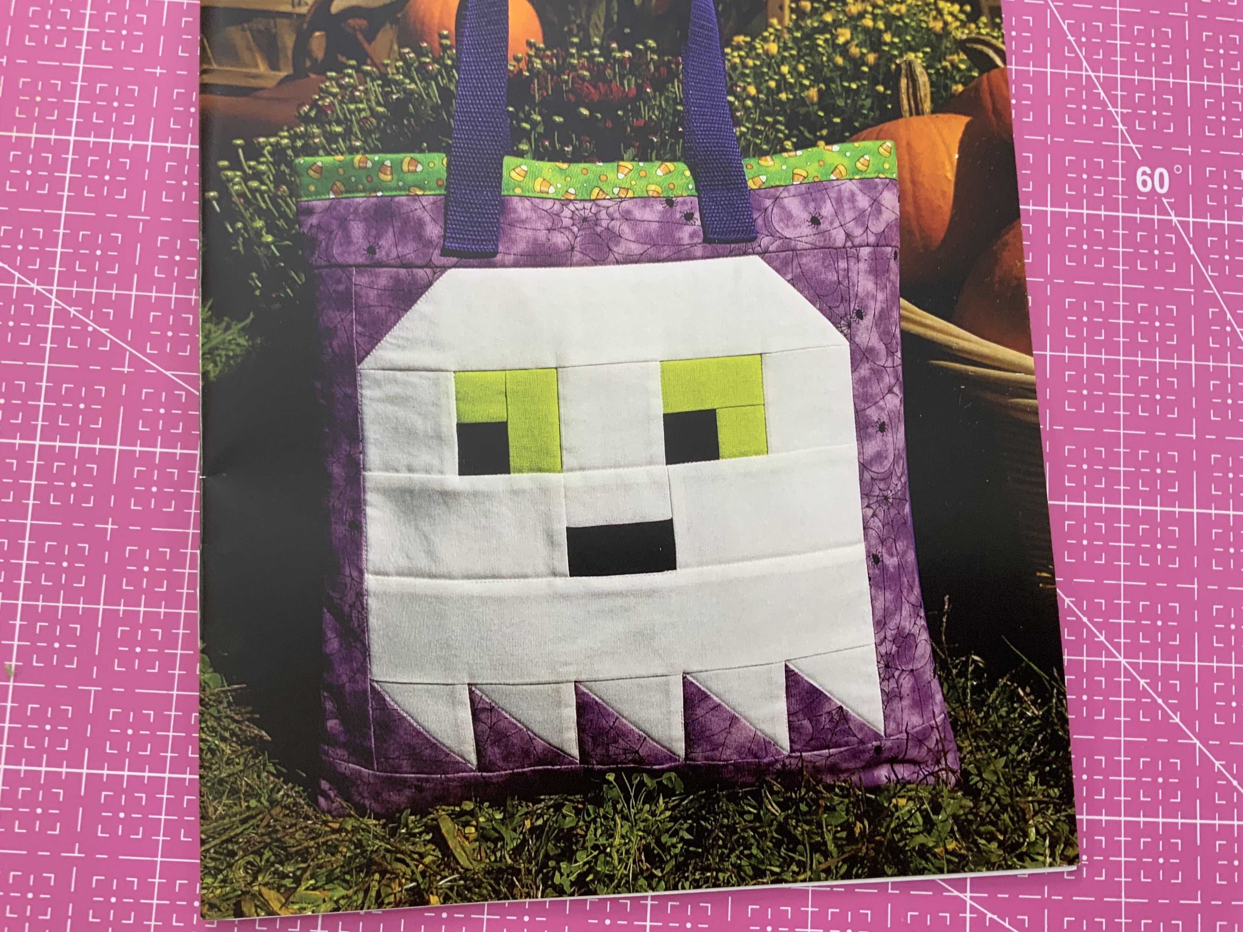 Ghost tote quilt pattern with a white ghost face and purple border tote bag with green handles.