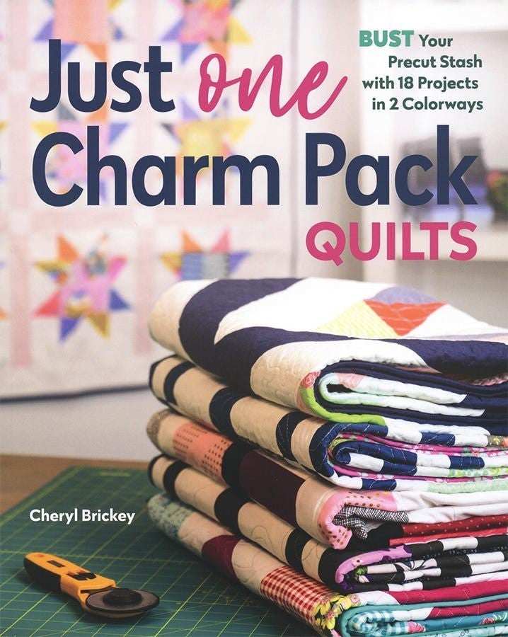 Just One Charm Pack Quilts book cover with stacked colorful quilts and sewing rotary cutter on table