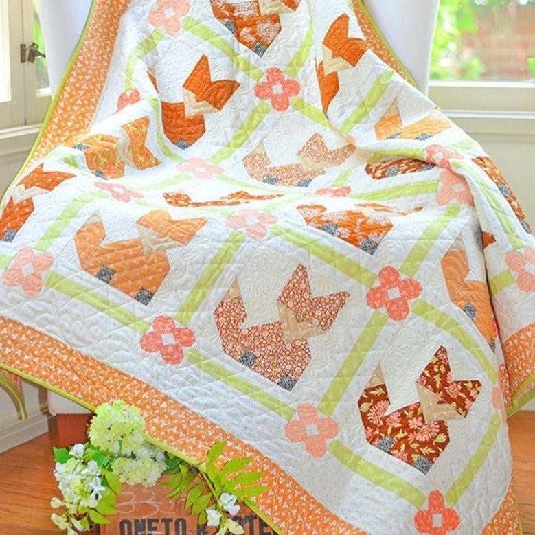 Francesca Quilt Kit featuring orange and cream floral patterned quilt draped over a chair with flower accents and a green plant nearby