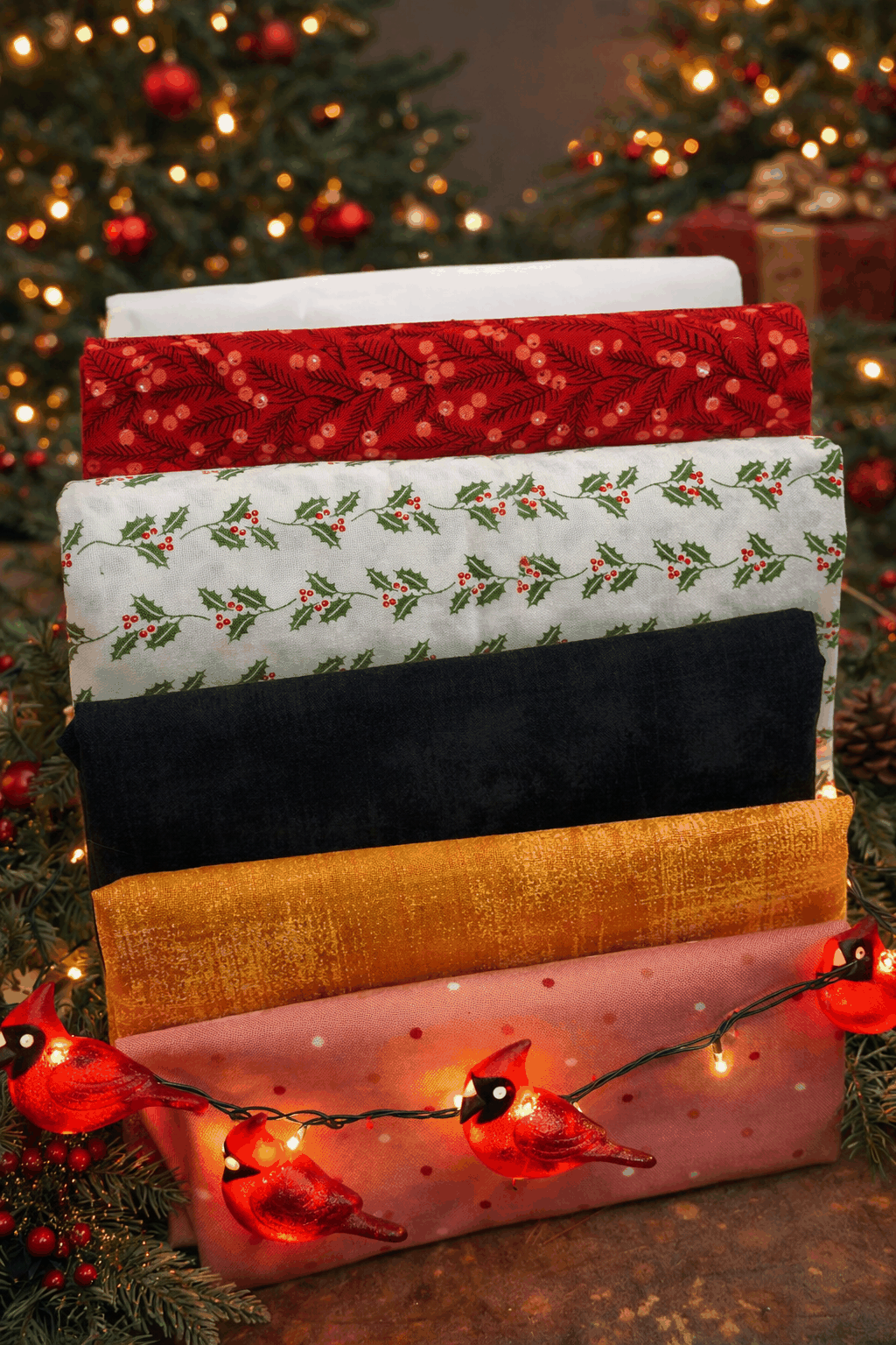 Advent Box Finishing kit fabrics in cardinal red, holly print, black, gold, and pink with cardinal lights background