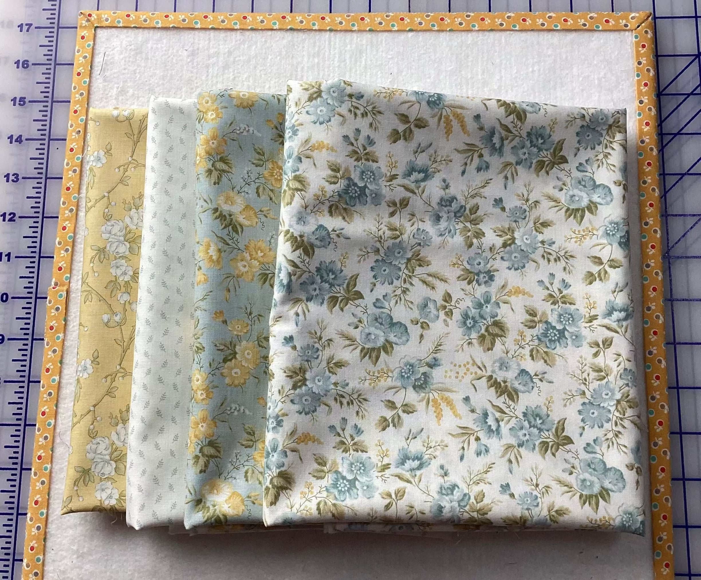 4-yard quilt fabric pieces with floral patterns in blue, yellow, and green tones stacked on a measuring mat