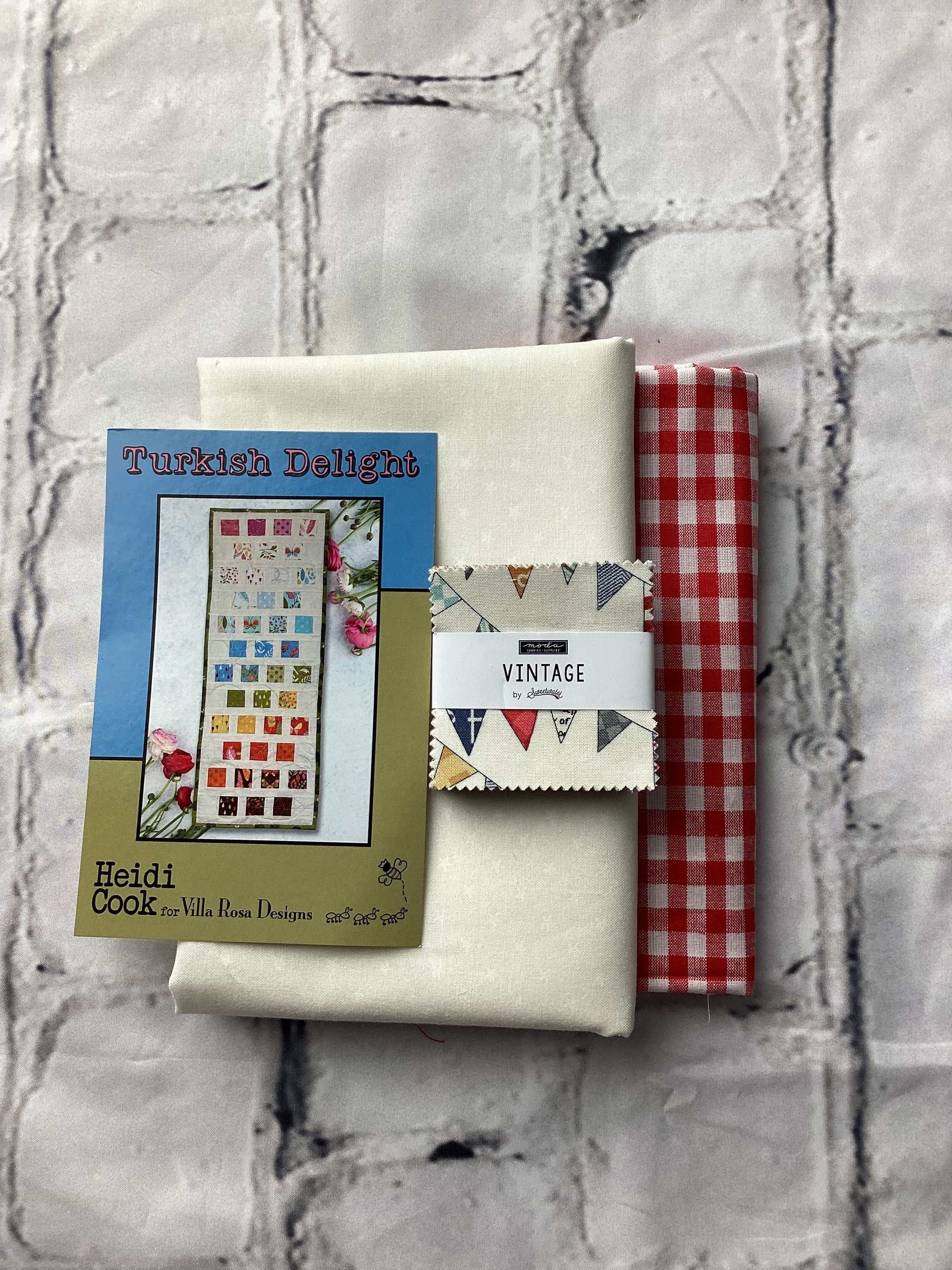 Turkish Delight quilt kit with vintage fabric by Sweetwater and red gingham fabric on a textured gray surface