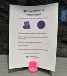 Pattern Stand Pink by Purple Hobbies LLC holding sewing patterns upright with weighted base for hands-free viewing