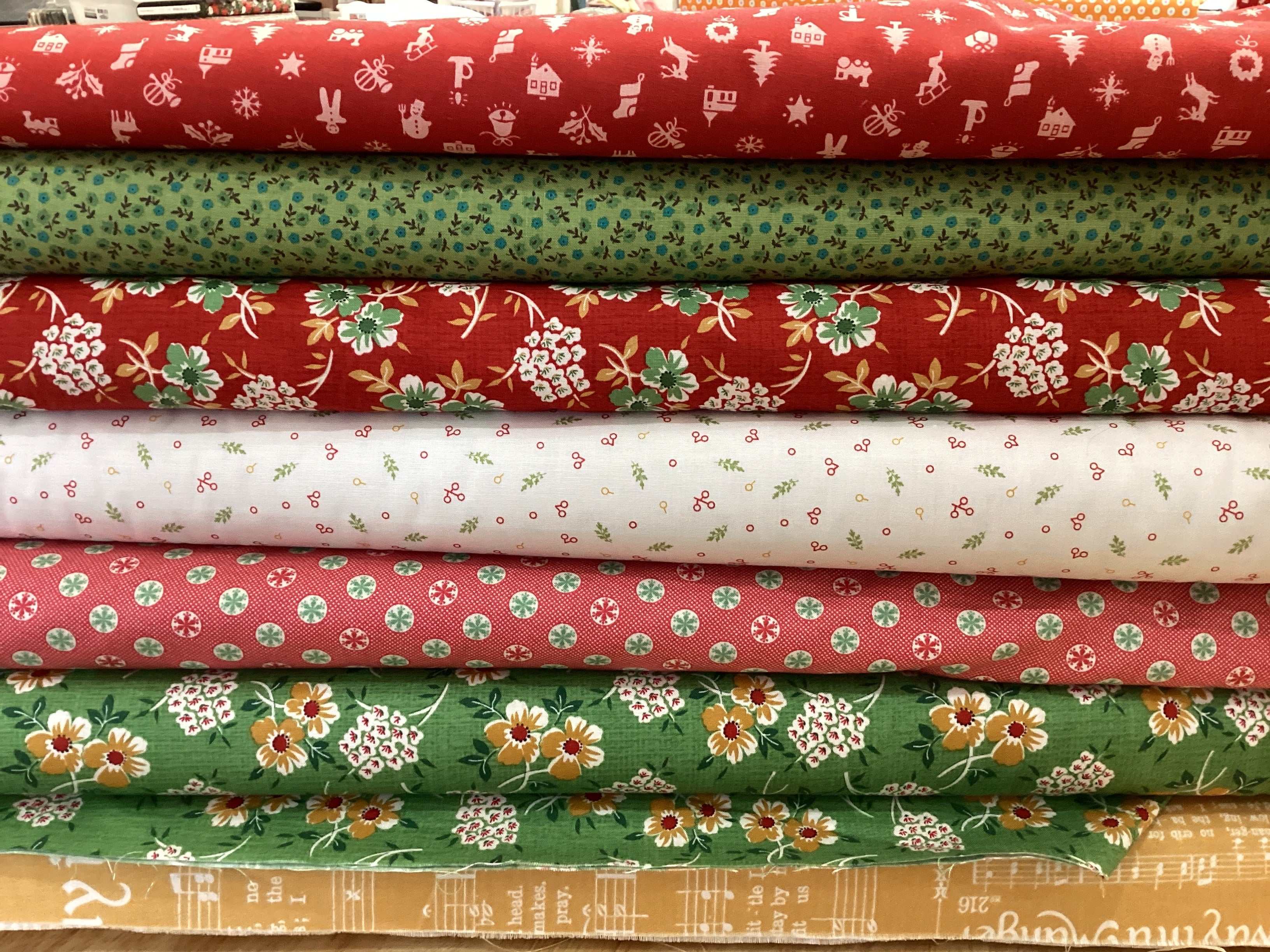 Stack of colorful floral and patterned quilting fabrics in red, green, white, and mustard tones for M50 Island Hopping Kit